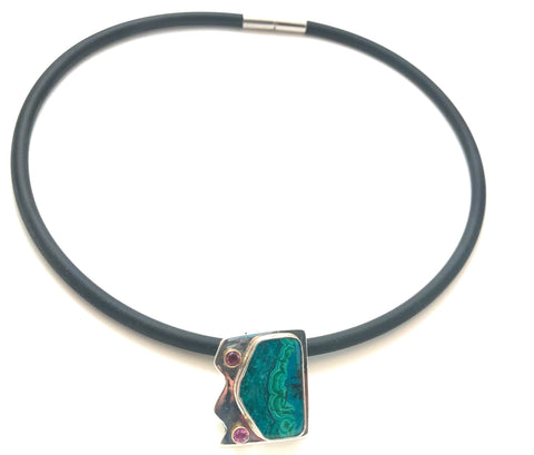 A pendant that is curved with zig zag lines and straight edges. The azure malachite stone is silky and accented with pink sapphires.