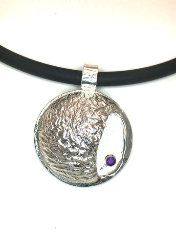 1 1/4" round diameter of reticulated silver with the texture of a mountain range.  Includes a bright purple amethyst in a gold tube setting.   The overall shape is a circle with a small open side-pocket.   