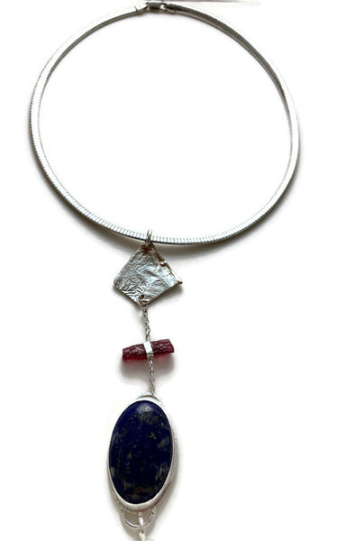 Pendant with three components: a beautiful navy blue lapis lazuli oval flecked with gold veining, a rough dark pink tourmaline and a free form reticulated silver slice. Hung from a 16" sterling silver smooth Omega chain. Pendant can be worn in either direction.