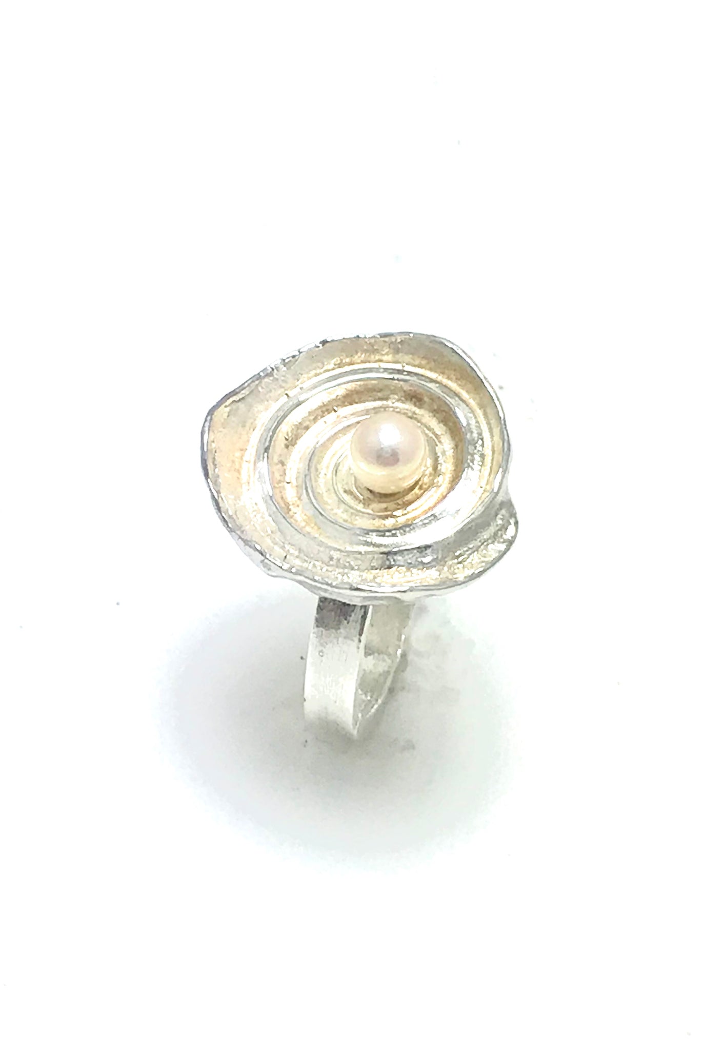 A ring made from a sea shell with the spiral cavities of the shell shining in sterling silver and a white pearl in the middle.