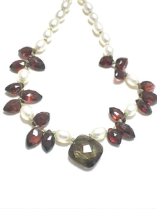 A pearl knotted necklace of white potato shaped pearls with marquise shaped red garnets and a focal point of one andalusite.   The andalusite is shaped as a rounded rectangle.   It is green with flashes of orange and lilac.
