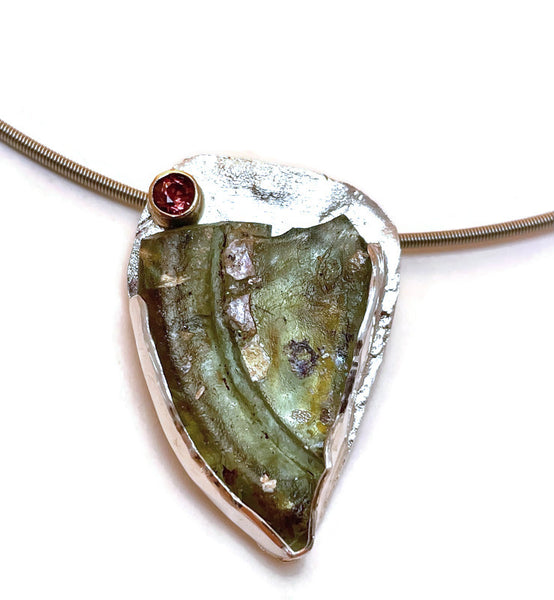 Close-up photo of the pendant showing the green color of the Roman glass shard and the purple red garnet in a 14KY gold setting.