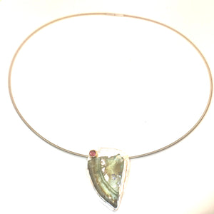 A free form pendant of sterling silver that is set with a 2000 year-old Roman glass shard from Israel.    The shard shows the beautiful rainbow of iridescence colors from minerals in the ground. Tactile texture. A purple/reddish garnet is set at the top to accent the green color of the Roman glass.   Price includes an 18"L sterling silver cable with safety clasp.
